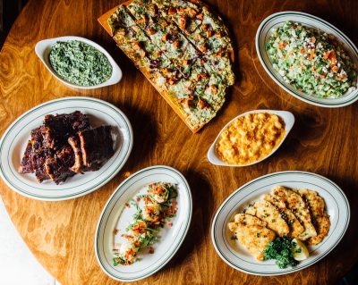 Several plates of food such as ribs, pizza, and salads