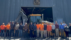 A photograph of the public works employees lined up in front of a warehouse and a front loader.